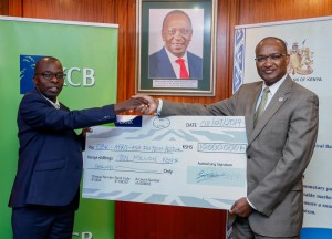 KCB Bank Chief Operating Officer, Samuel Makome hands over a dummy cheque of Kshs 10 million to CBK Governor, Dr Patrick Njoroge. Photo, supplied